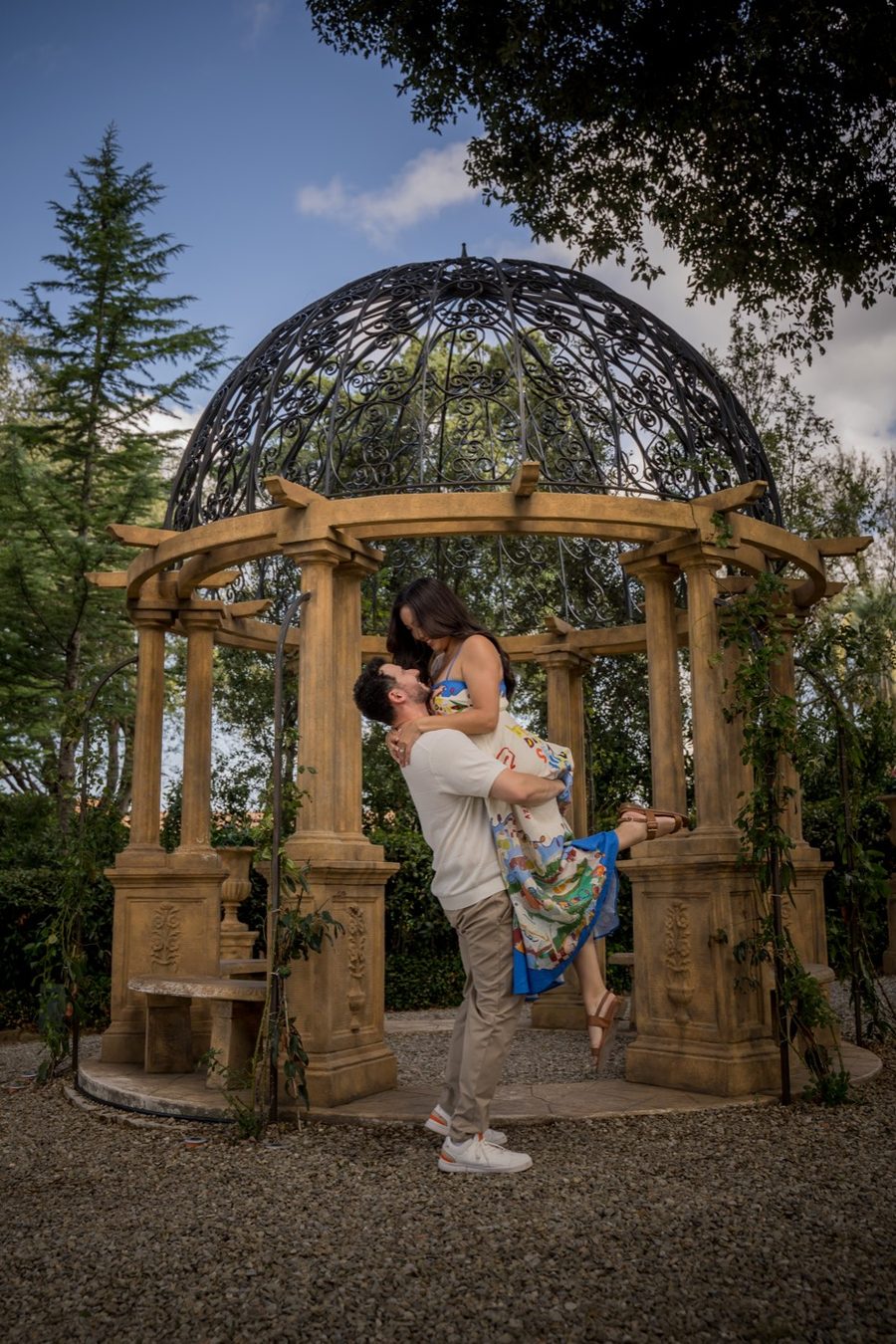 Anthony lifting Jennifer beneath a wrought-iron garden gazebo